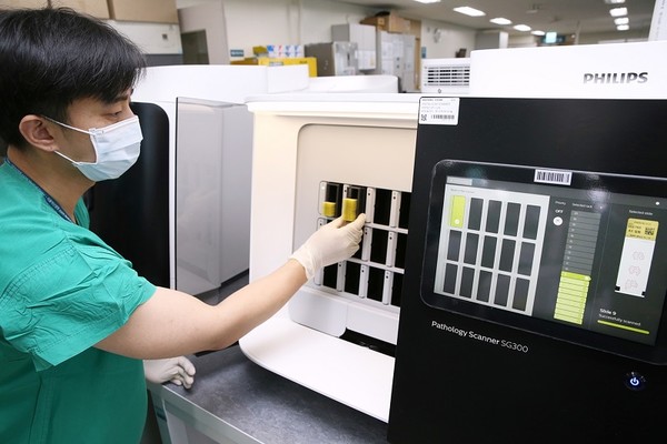 서울아산병원 병리 검사실 직원이 검체 슬라이드를 디지털 스캐너에 넣고 있다. 검체 슬라이드 스캔 영상은 서울아산병원 전자의무기록시스템(EMR)을 통해 자동 분류돼 담당 병리 판독 의사의 모니터로 전송된다.